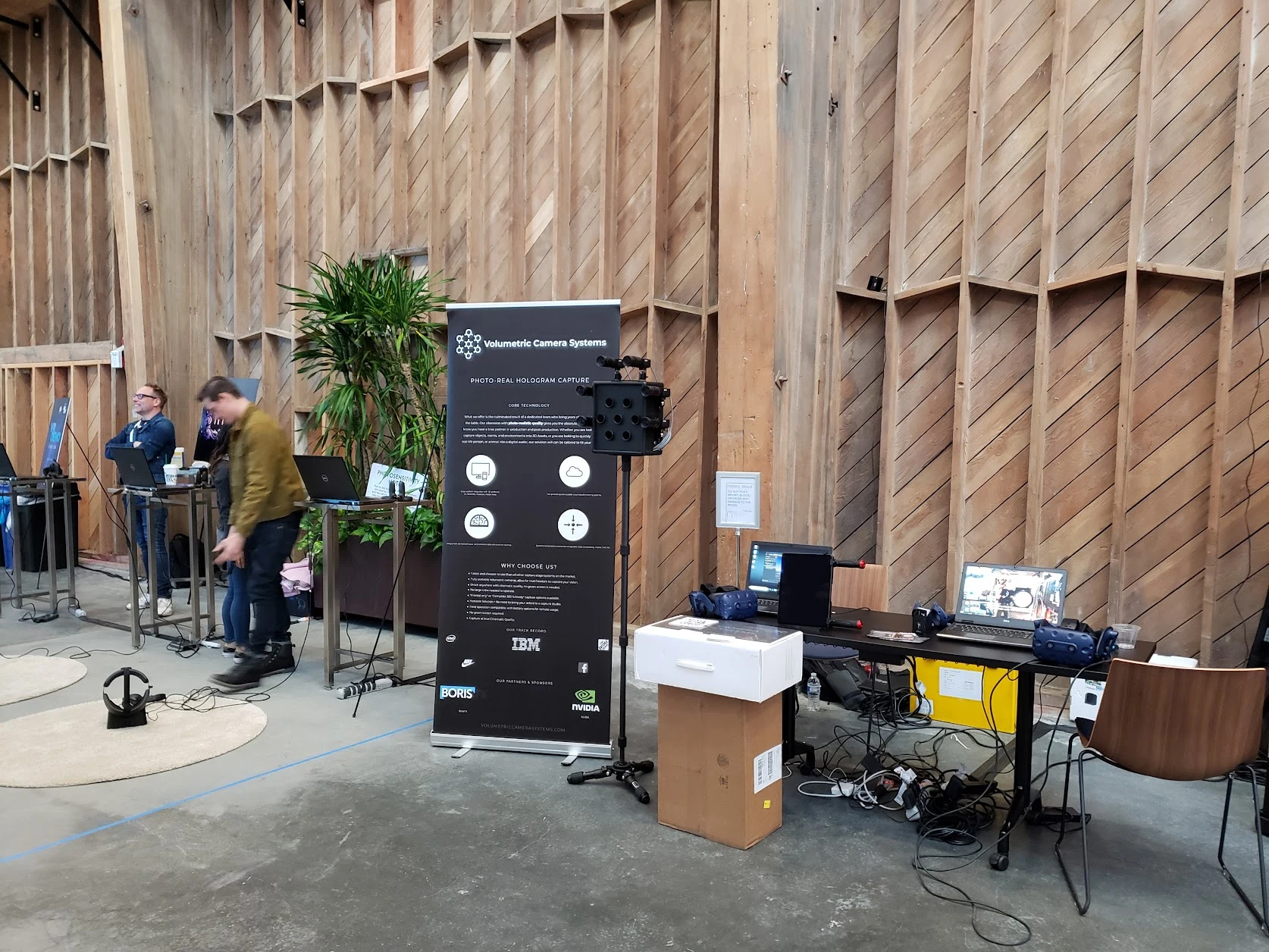 VCS banner, compact camera and display in a wood-walled event space.